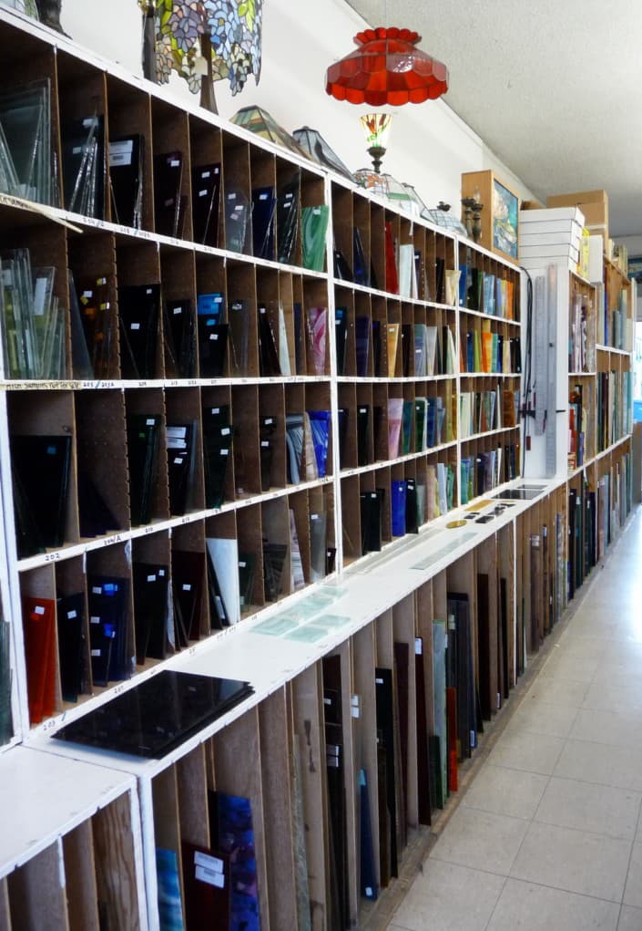 Glass wall display showing colored stained glass sheets at the studio